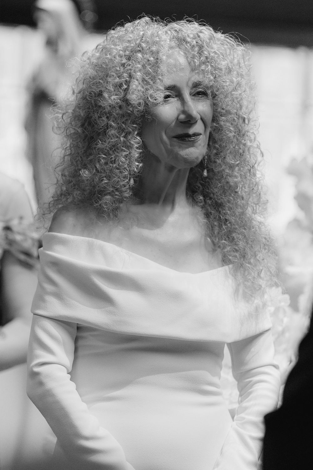 A sequence of black and white photos showing a person with voluminous curly hair wearing an elegant white off-shoulder dress.