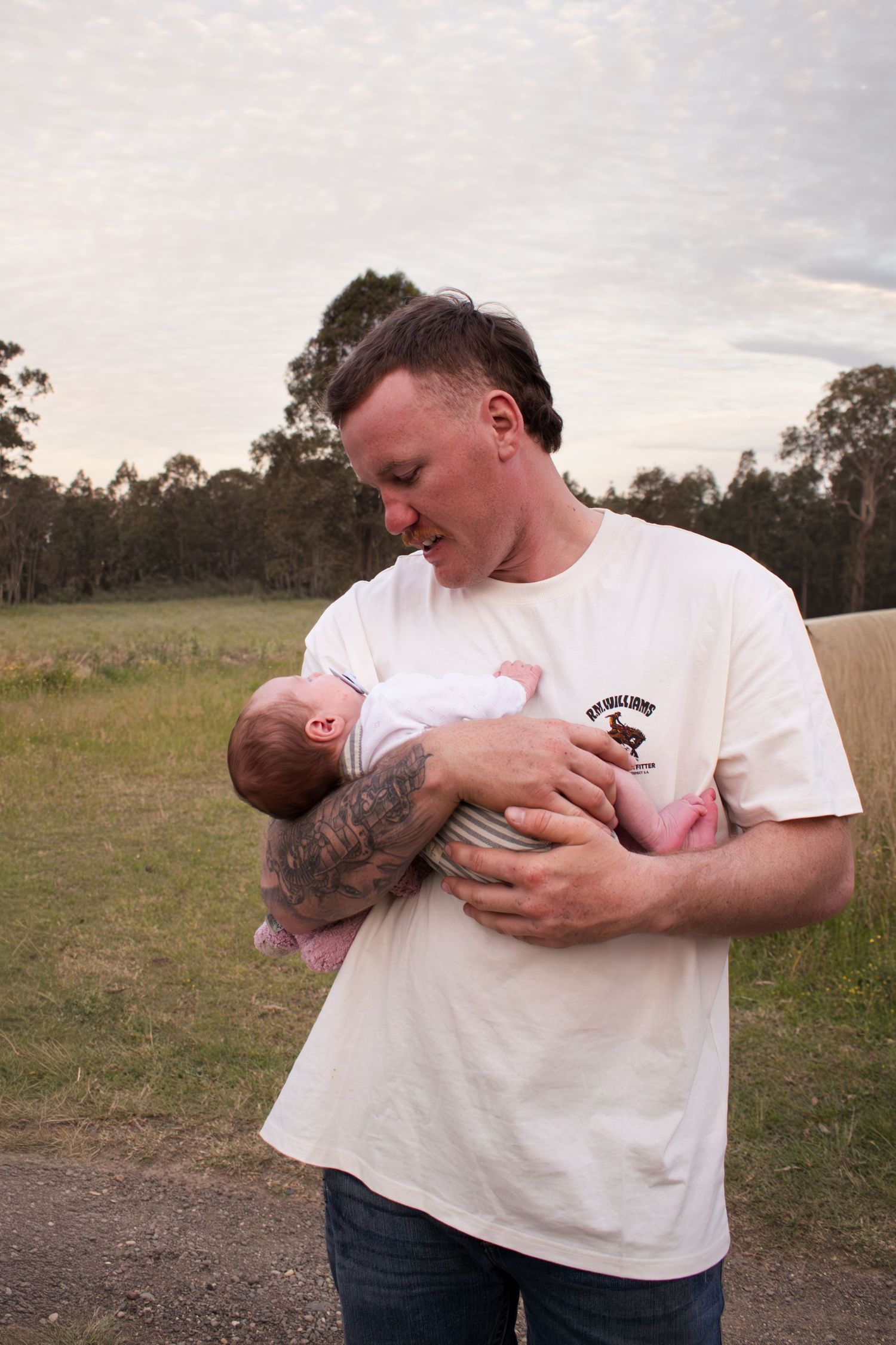 Dad holding newborn baby in grassy field during a golden hour newborn photoshoot in Maitland NSW