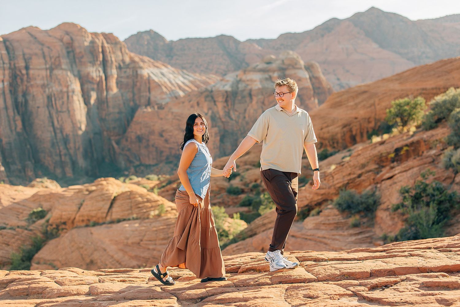 Two people hiking together on red sandstone formations in a scenic desert canyon landscape.