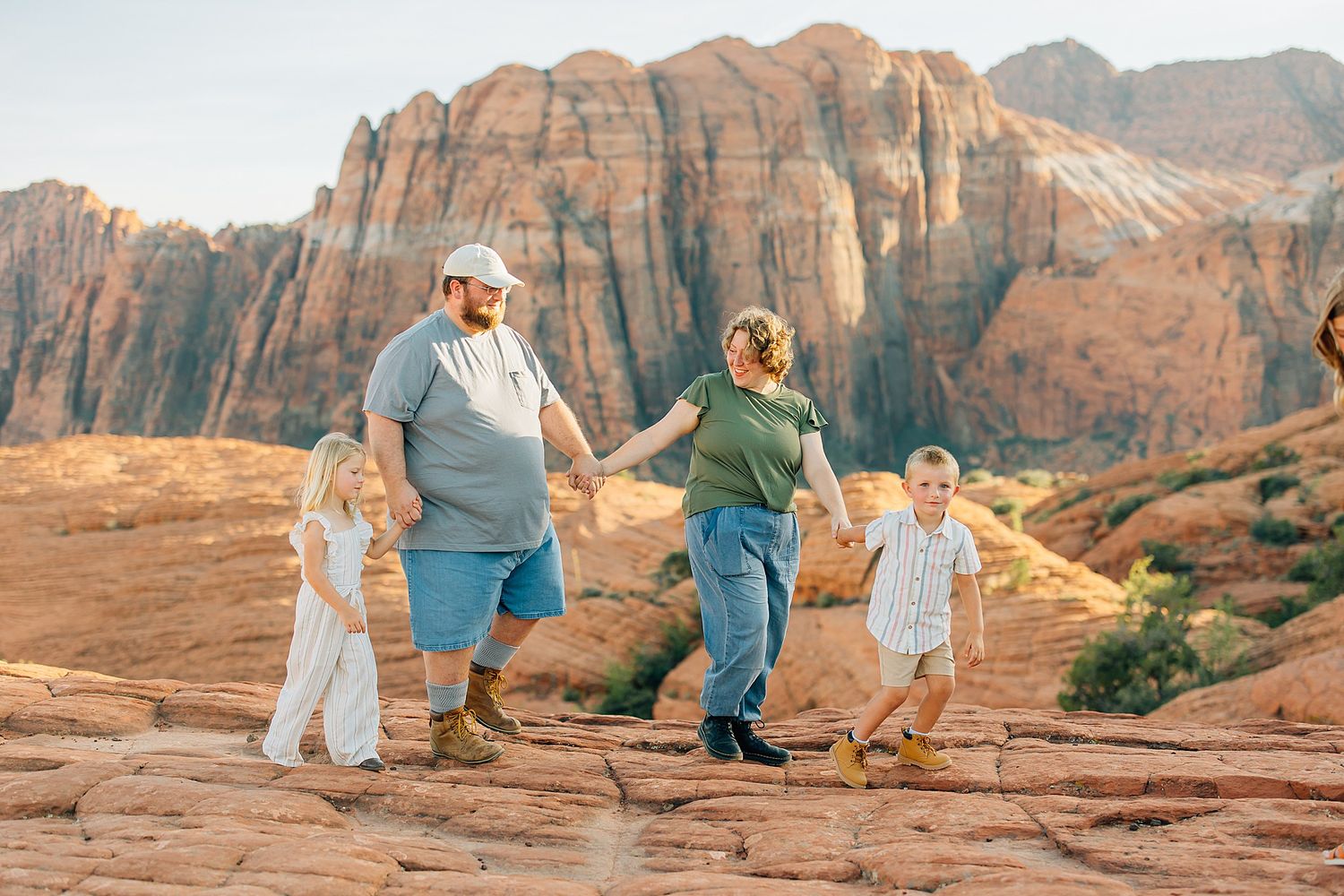 People enjoying a scenic moment together on red rock formations in a desert landscape at sunset.