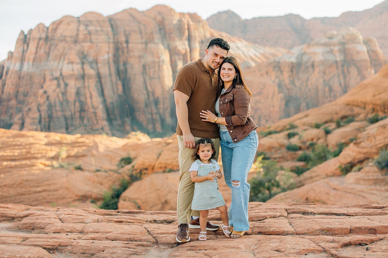 Family enjoying a scenic photo session among towering red rock formations in the desert landscape at sunset.