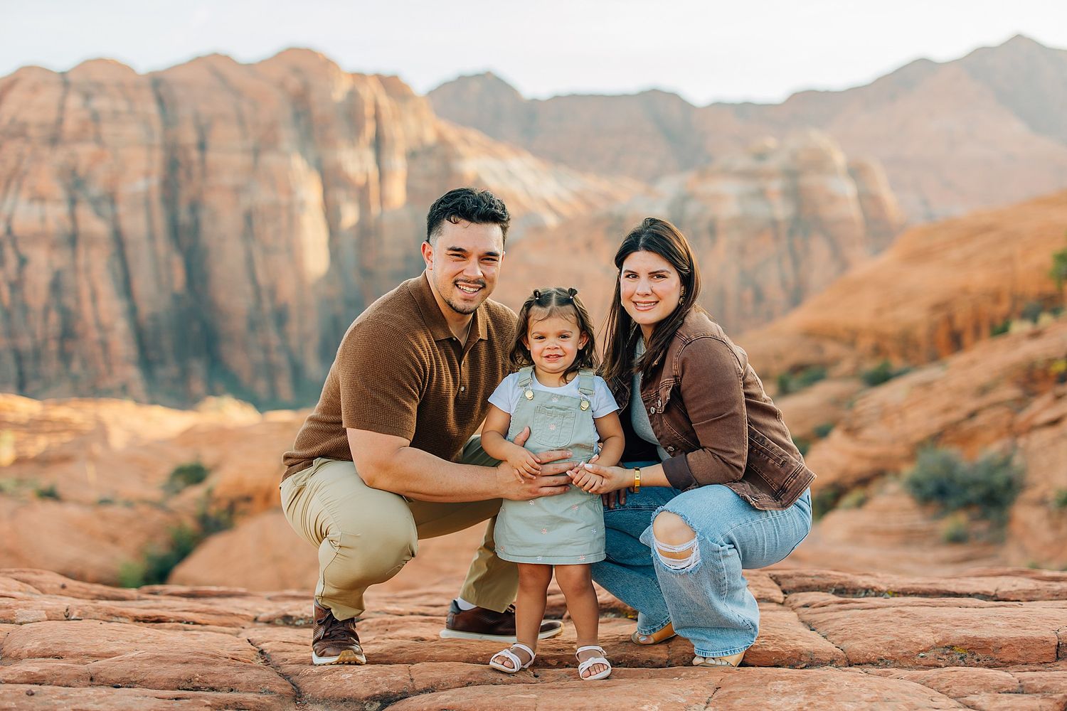 Couple shares romantic moments against stunning red rock formations in desert landscape at sunset.