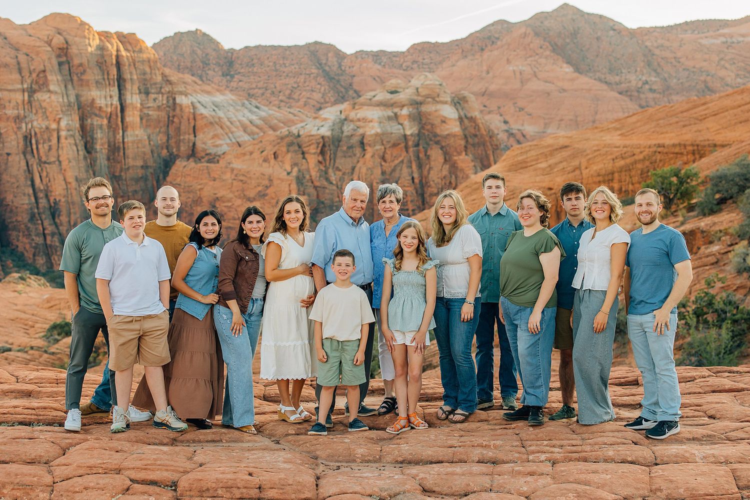 Large family group poses together against stunning red rock formations in desert landscape at sunset.