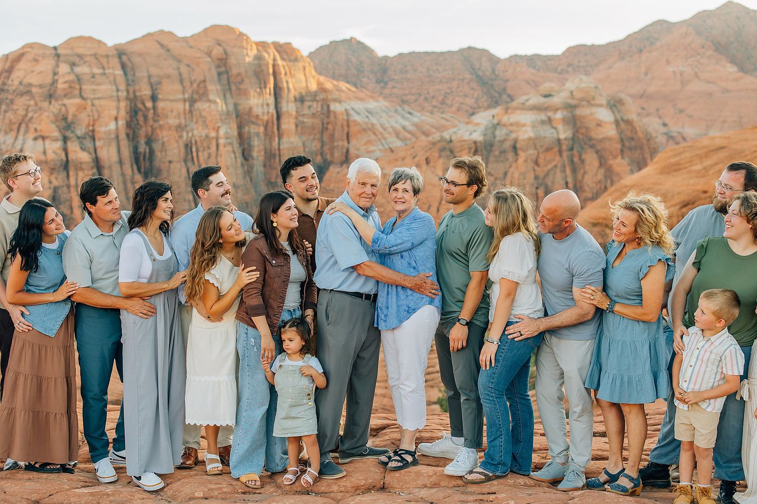 Large group portrait with people wearing coordinated blue and gray outfits against red rock desert scenery.
