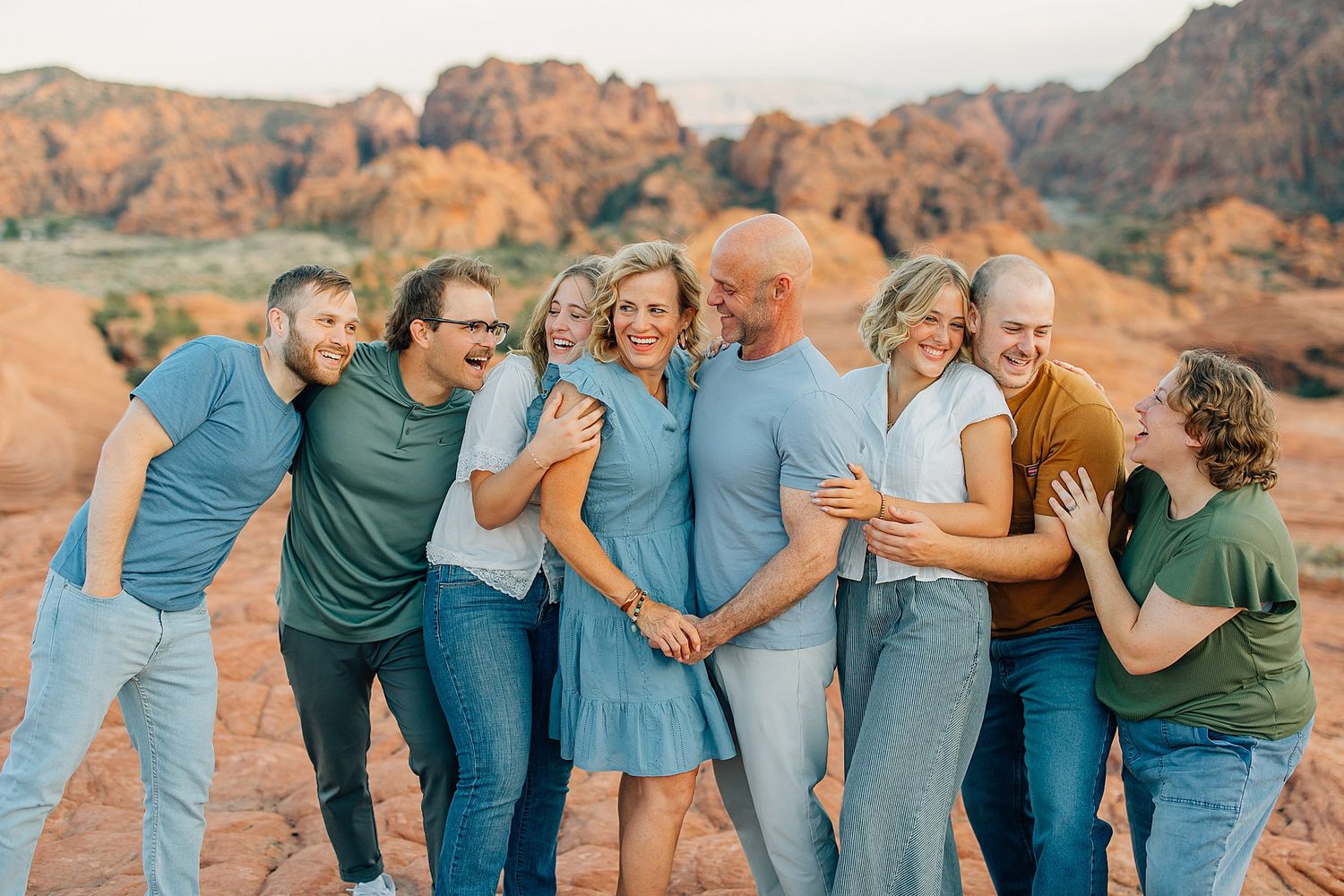 A group in coordinated blue and green outfits laughs together against a backdrop of red rock formations in the desert.