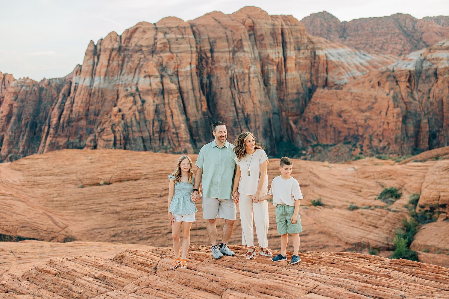 Family wearing coordinated mint and white outfits poses against stunning red rock formations in the desert landscape.