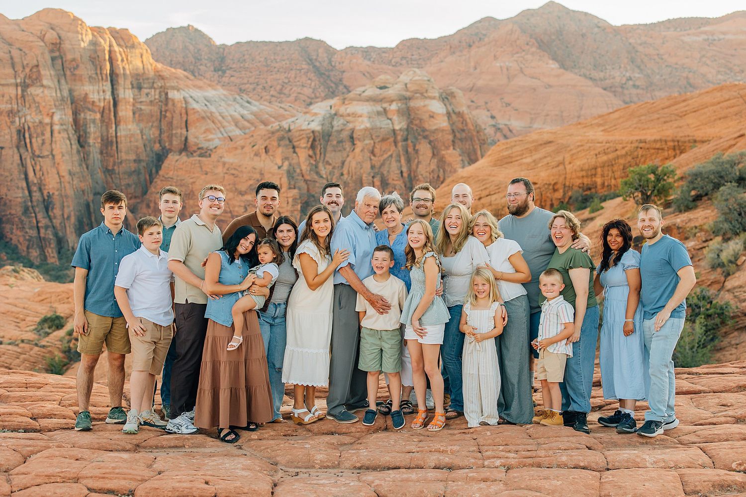 Extended family group wearing coordinated blue outfits poses together against red rock formations in desert landscape.