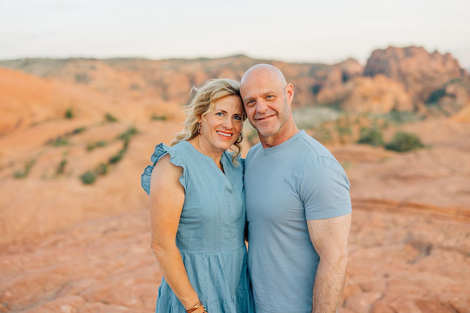 Couples in matching light blue outfits embrace while posing against scenic desert rock formations.