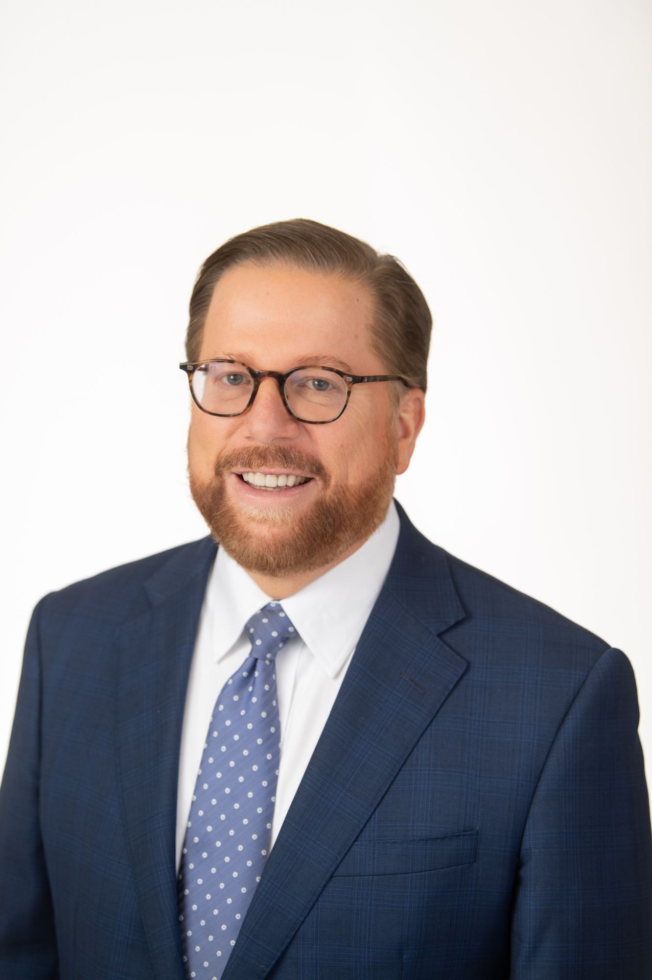 Professional headshots of a person in a navy suit and polka dot tie against white background.