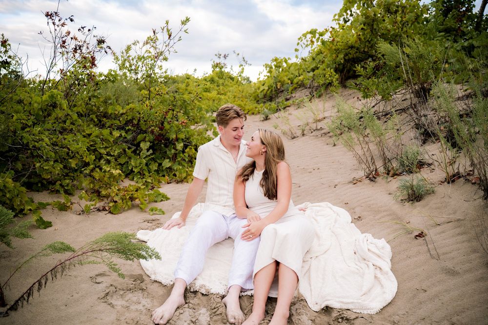 Romantic beach wedding photography session with couple sitting on sandy dunes at sunset.