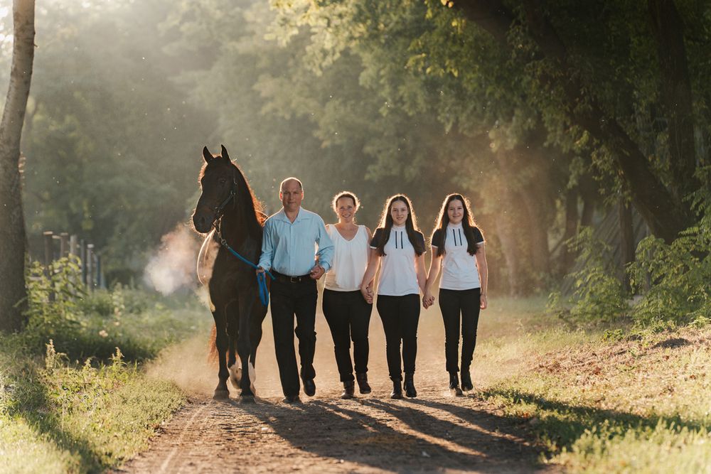 A group of people walking together with their horse on a sunlit forest path during golden hour photoshoot