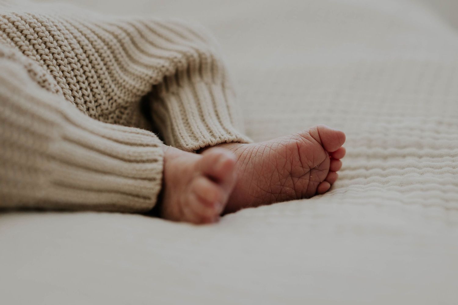 Close-up view of tiny baby feet peeking out from a cozy cream-colored knit blanket. Minneapolis newborn photographer.
