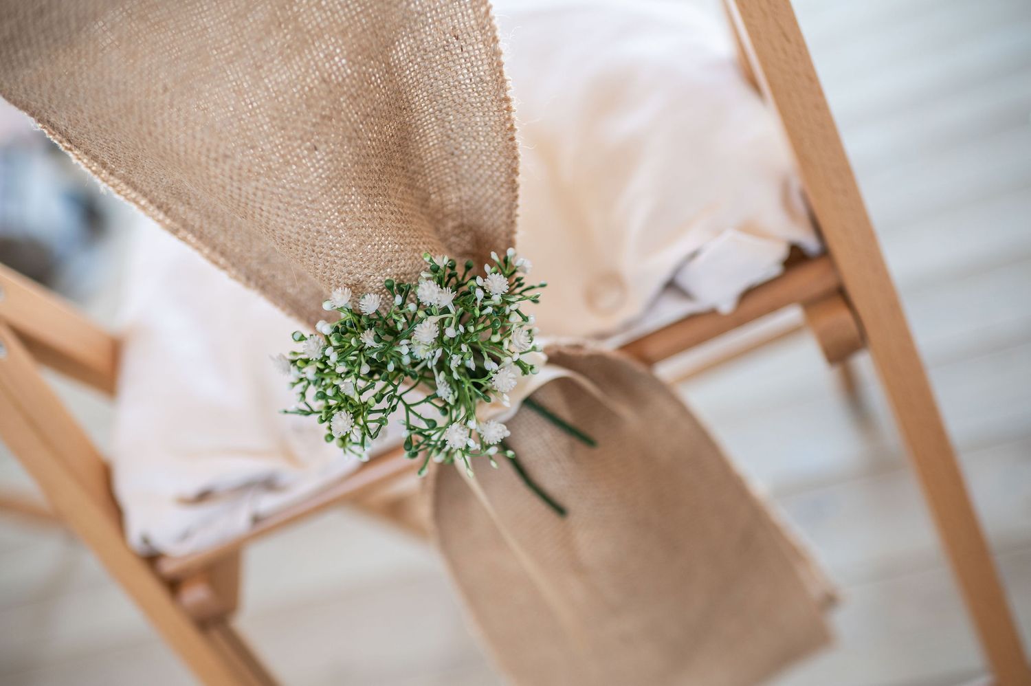 Close up shot of the back of a ceremony chair with a hessian tie and green and white decoration
