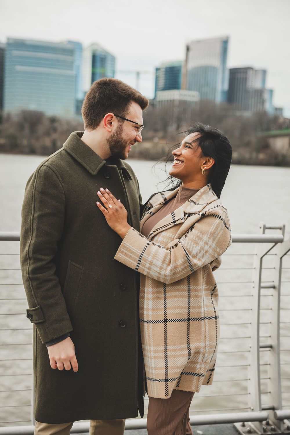 A couple shares joyful laughter while standing by a waterfront in Georgetown, a wonderful outdoor winter dc proposal location