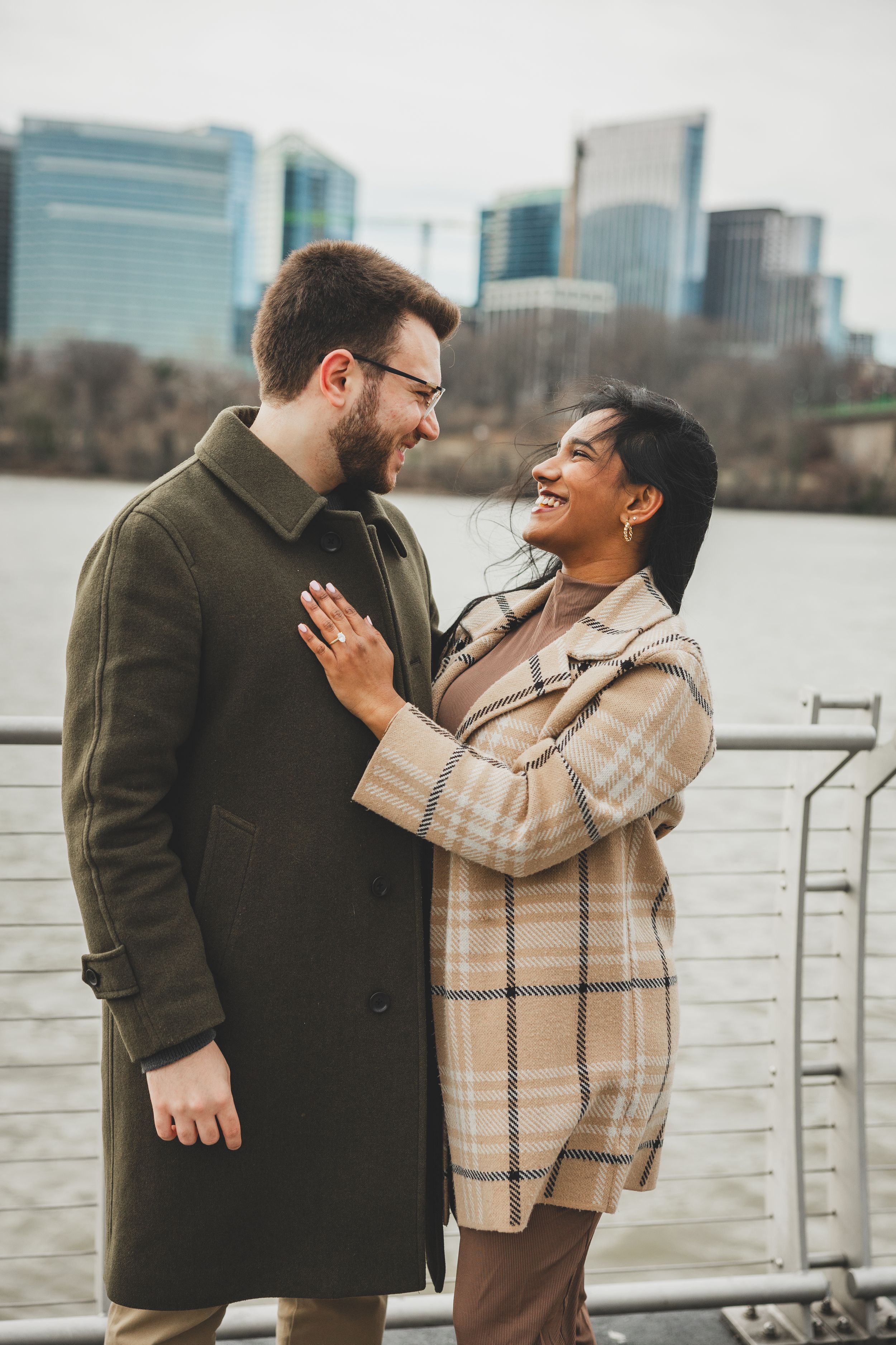 A couple shares joyful laughter while standing by a waterfront in Georgetown, a wonderful outdoor winter dc proposal location