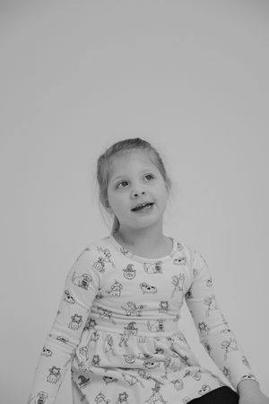 Black and white portrait of a child wearing a patterned dress against a plain background.