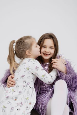 Two children in white and purple outfits share playful moments in a photo series against a light background.