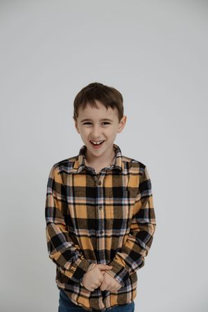 A young child in a yellow plaid flannel shirt stands against a white background with a cheerful expression.