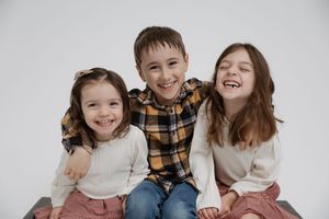 Cheerful family sitting together on floor in coordinated cream and brown outfits for casual photo session.