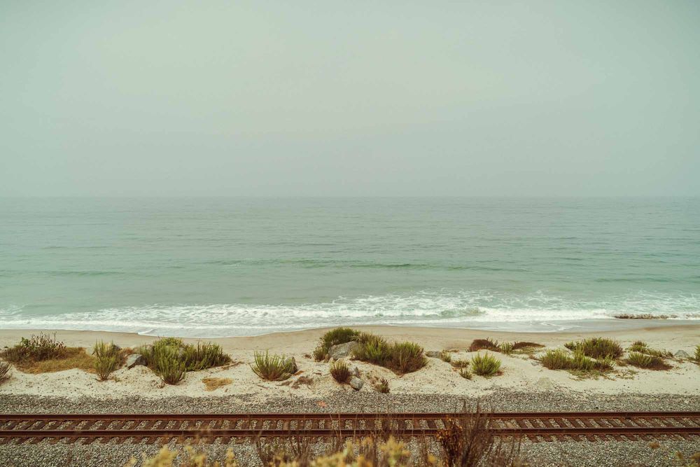 A panoramic view of a misty coastline with ocean waves crashing against a sandy beach and dunes.