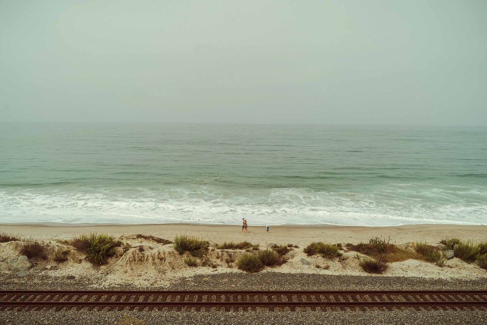 Scenic coastal landscape with railroad tracks running parallel to misty ocean waves on a cloudy day.