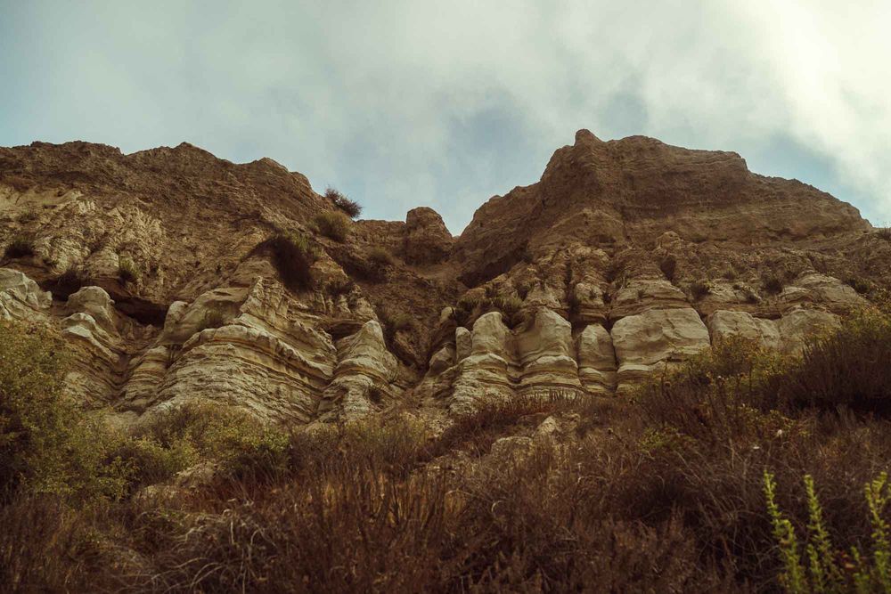 Rocky desert landscape with rugged mountain formations and cloudy sky in the background.