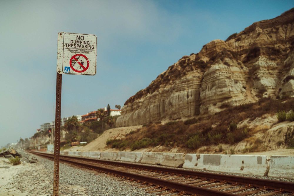 A series of seven vintage-style photos showing railroad tracks along a coastal cliff with warning signs and fencing.