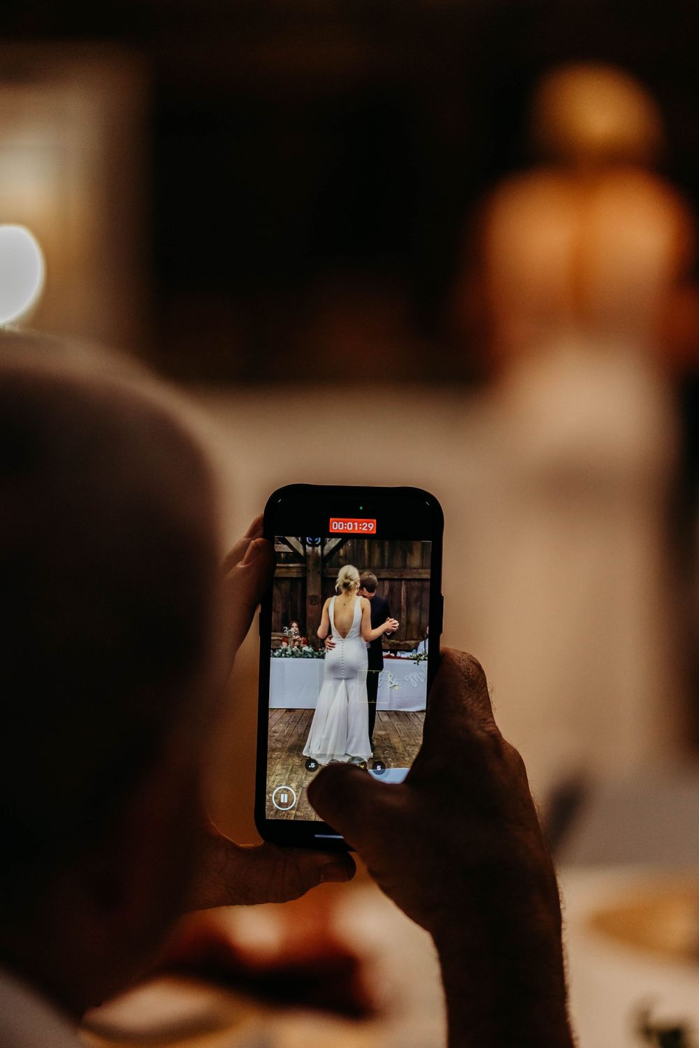 Guest recording bride and groom first dance on smartphone at elegant wedding reception.