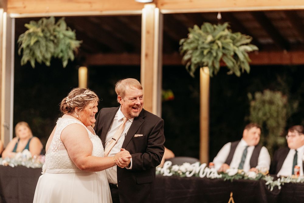 Bride and groom share a joyful first dance at their wedding reception under warm lights.