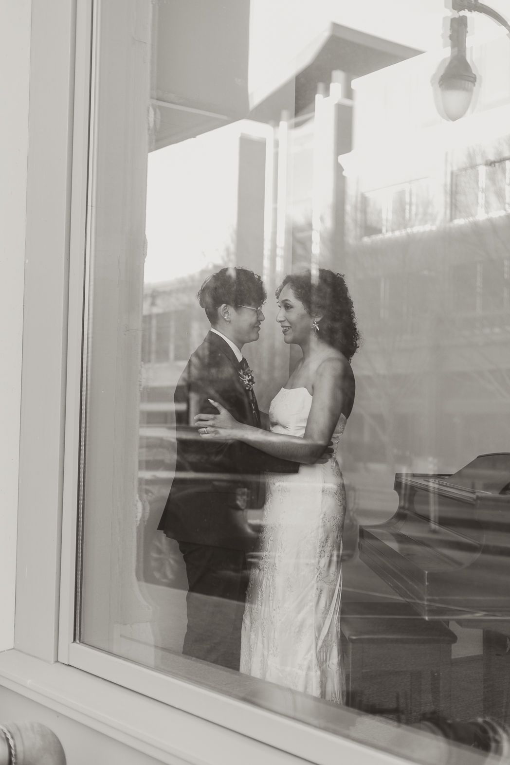 A black and white wedding photo series showing a couple in romantic poses by large windows.