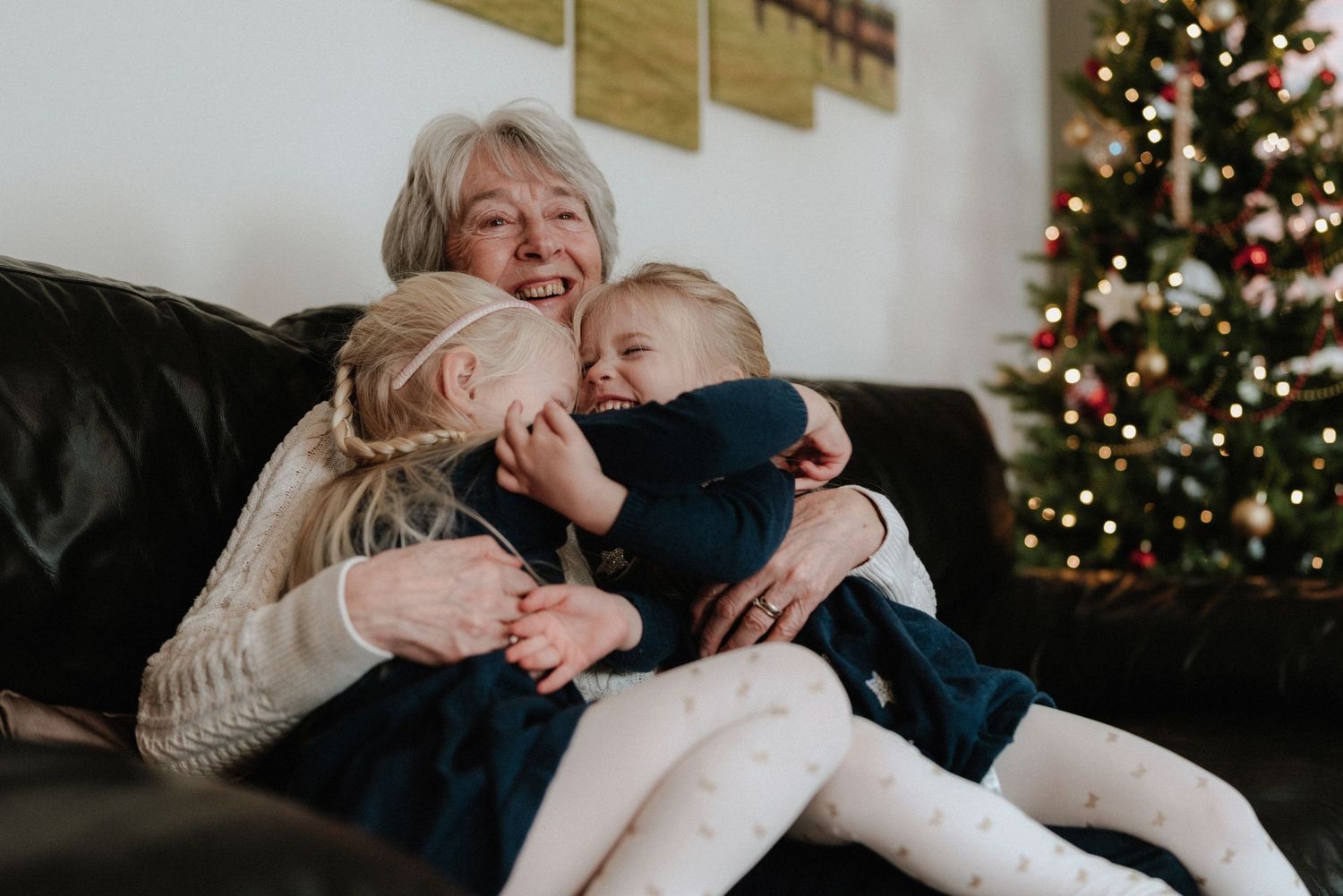 A joyful moment of cuddling and laughter on a leather couch with a decorated Christmas tree in the background.