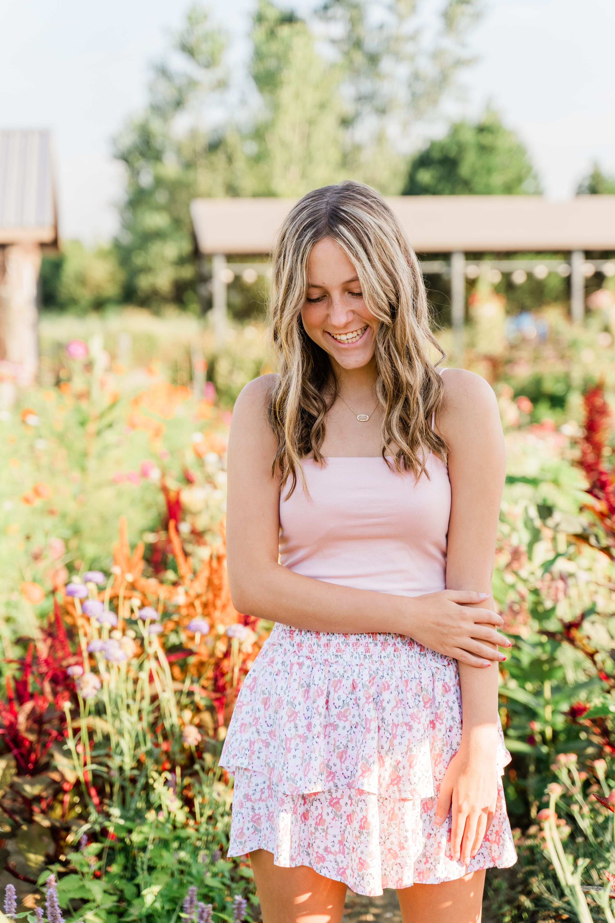 Person in pink top and floral skirt poses in a vibrant garden with colorful flowers and greenery in background.
