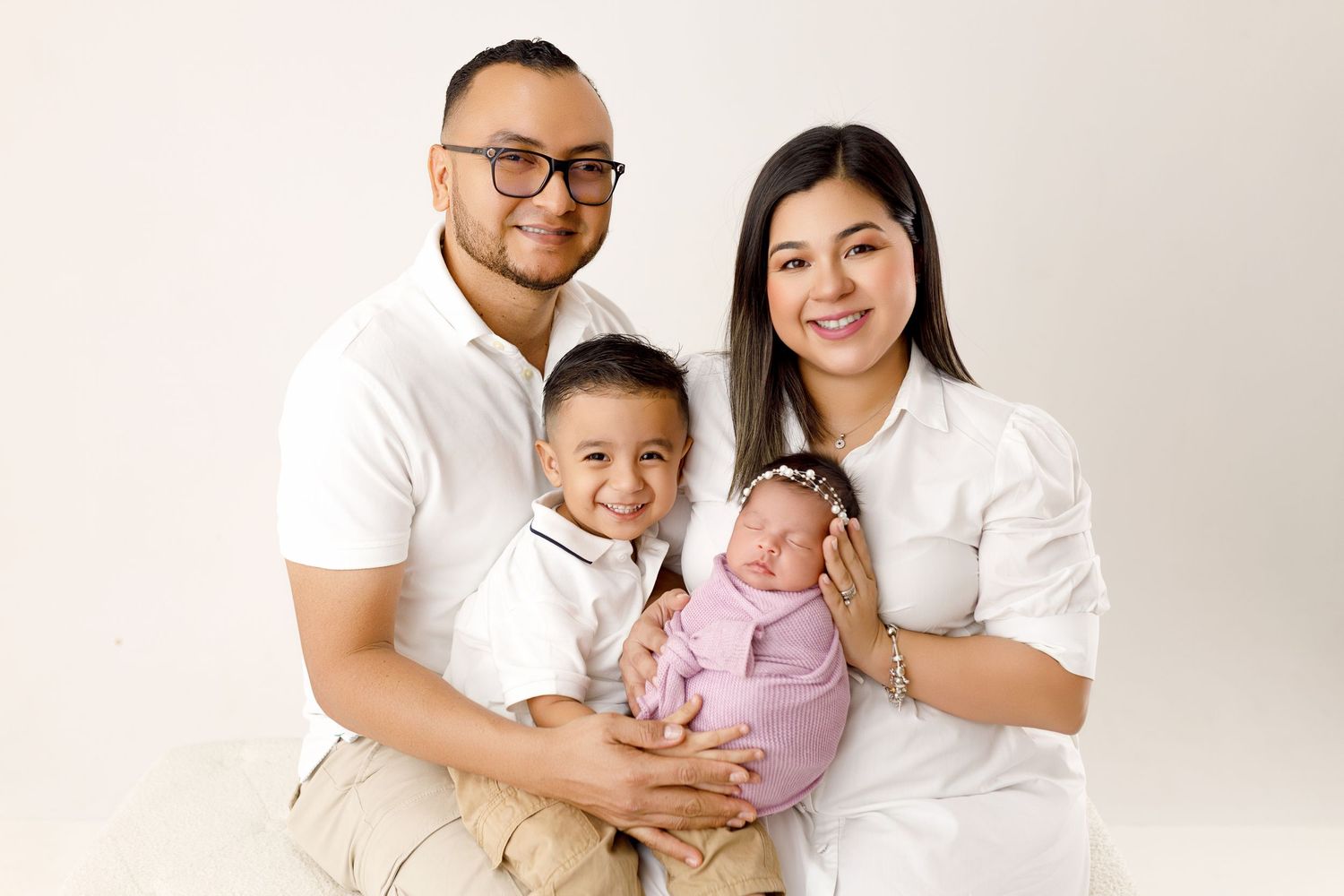 Family wearing coordinated white outfits poses together against neutral background for professional portrait session.