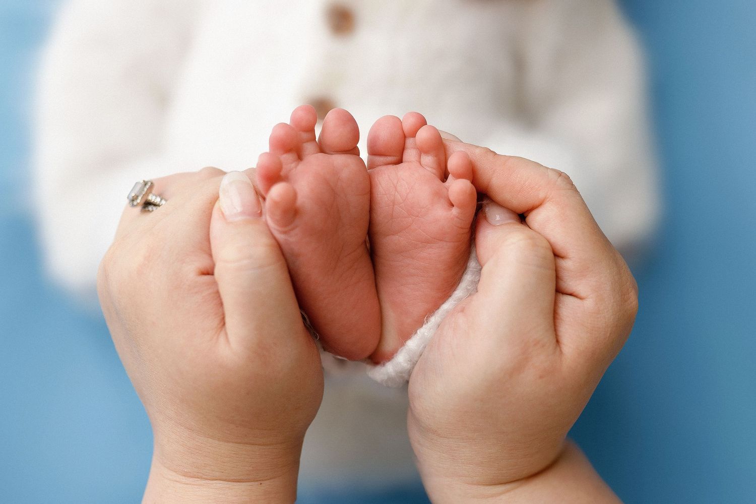 Adult hands gently holding tiny baby feet against a blue background.