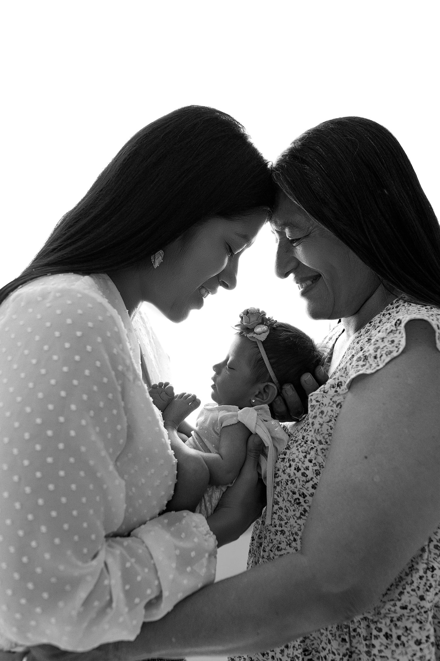 A tender black and white photograph capturing an intimate family moment between three generations sharing smiles and closeness.
