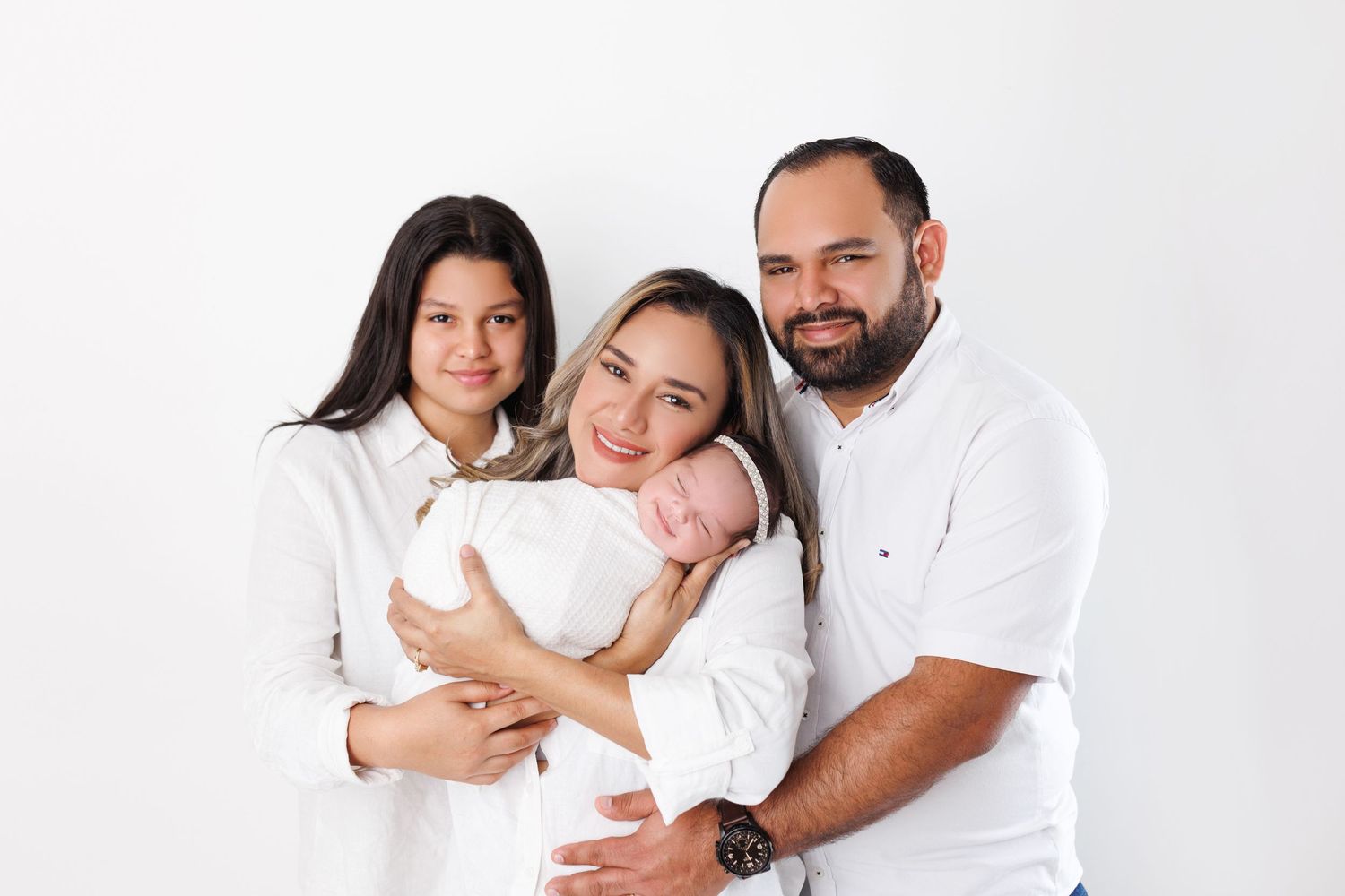 Family of three wearing coordinated white outfits against white background.