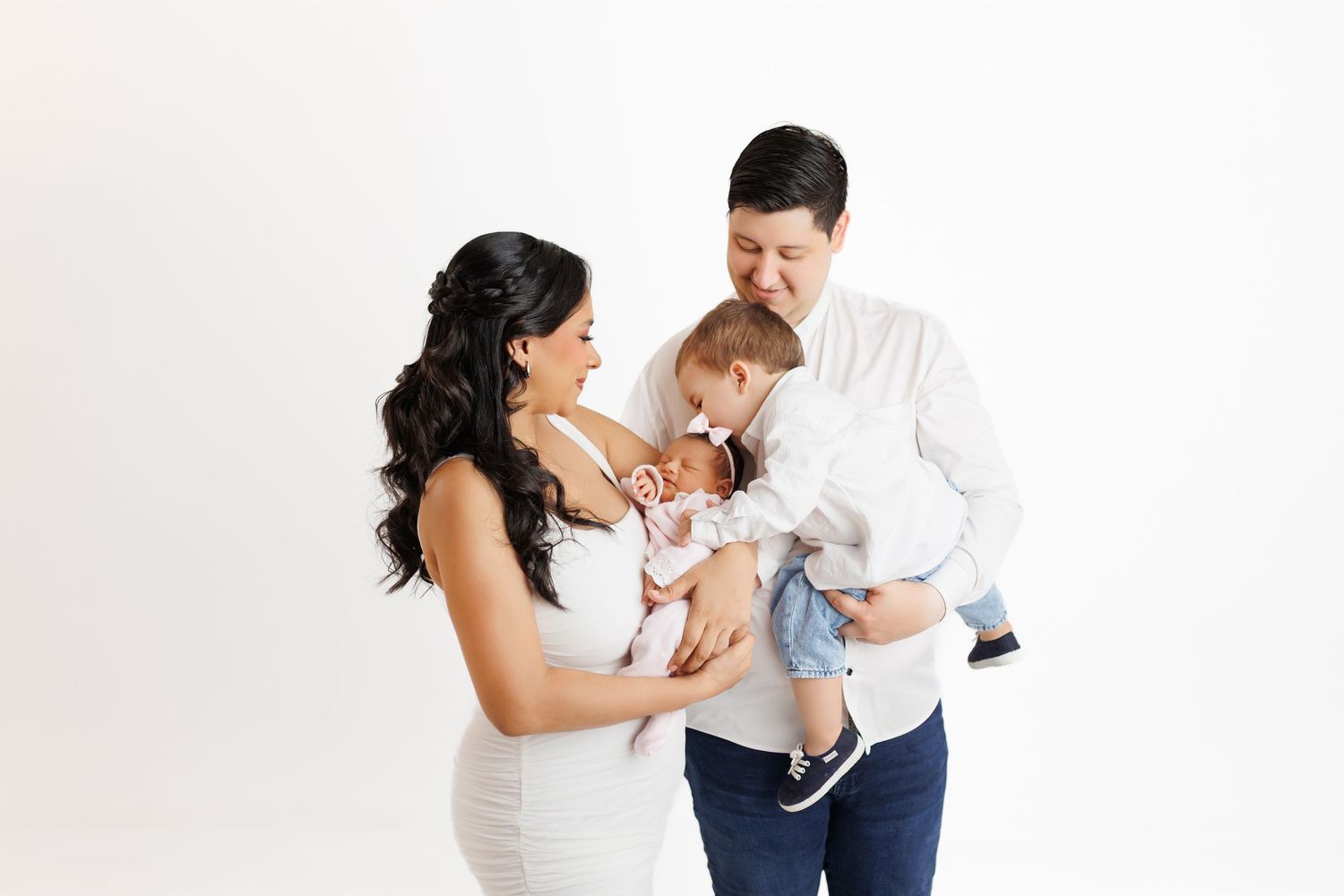 A couple in white and navy outfits holds and plays with a small white dog against a light background.