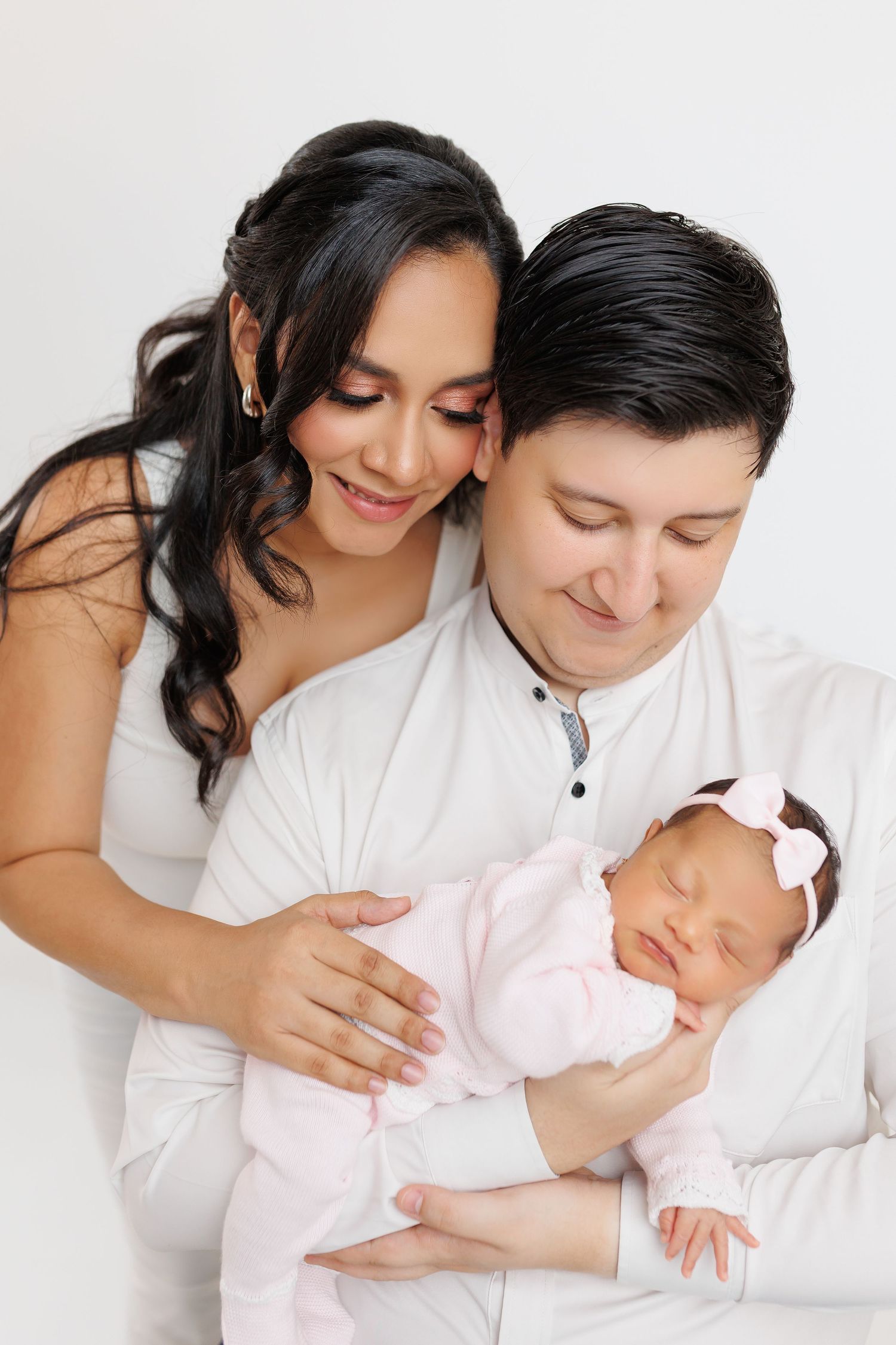 A tender family moment captured in a series of white studio photos showing parents bonding with their newborn baby.