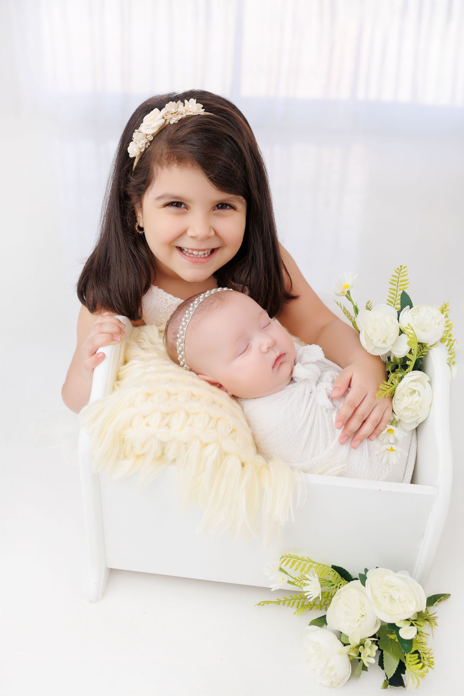 A child in a pale yellow dress poses with white flowers in a bright studio setting.