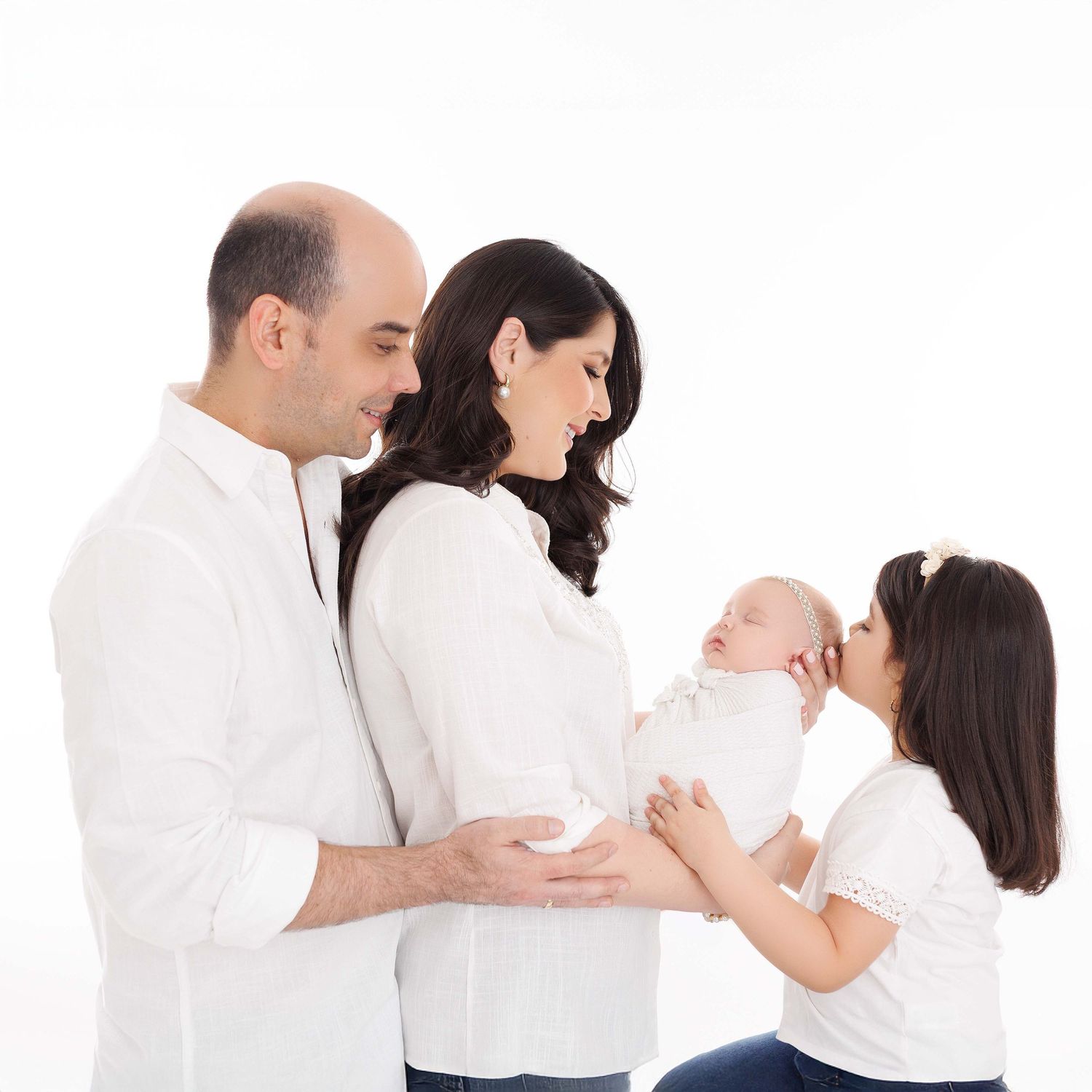 Family wearing white clothing poses together in a series of tender embraces against a light background.