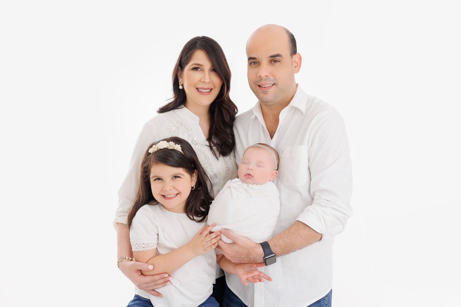 A family wearing white shirts sits together on a white background for a studio portrait session.