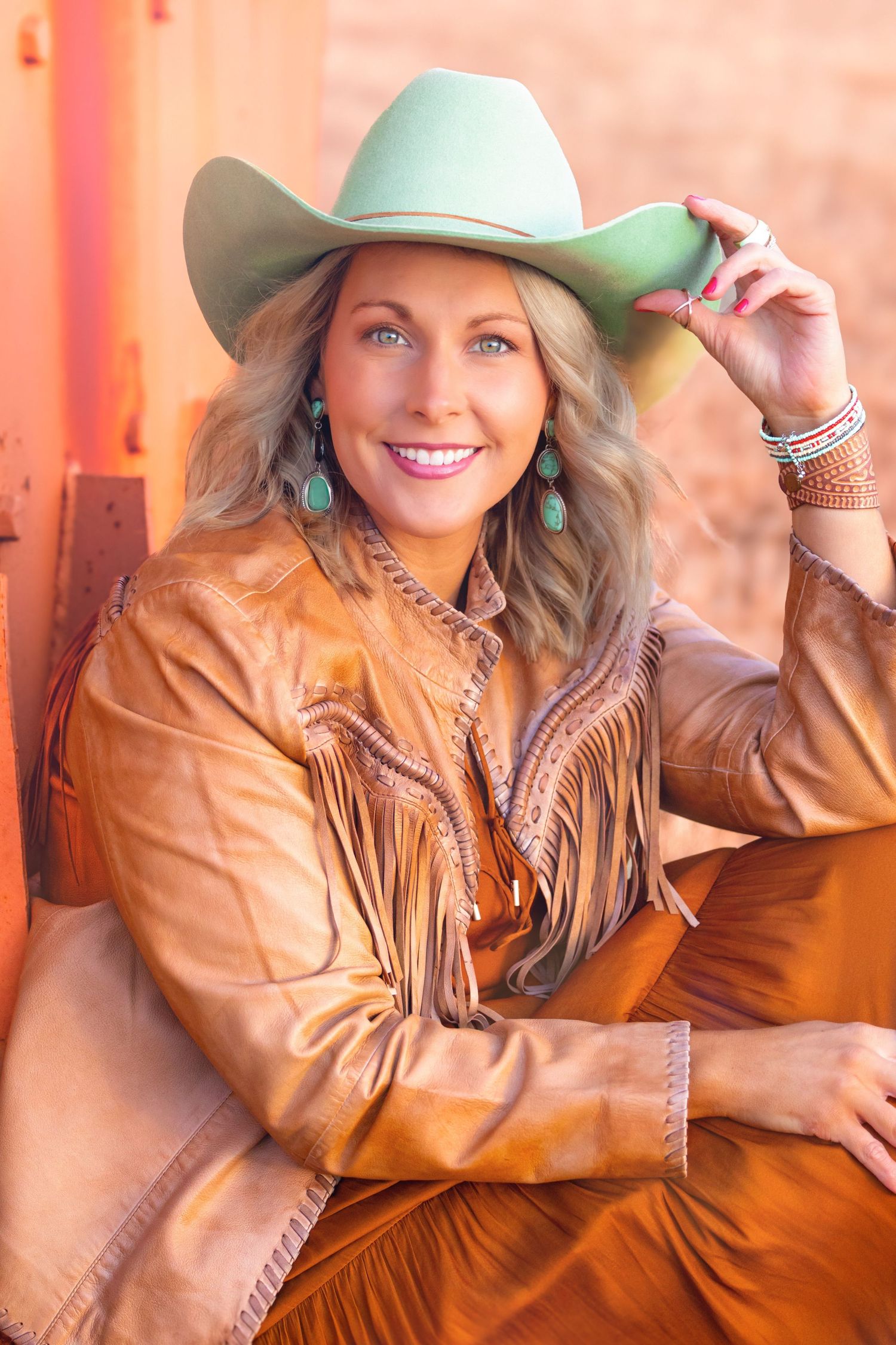 A person in a brown leather jacket and mint green cowboy hat poses in a series of photos with warm lighting.
