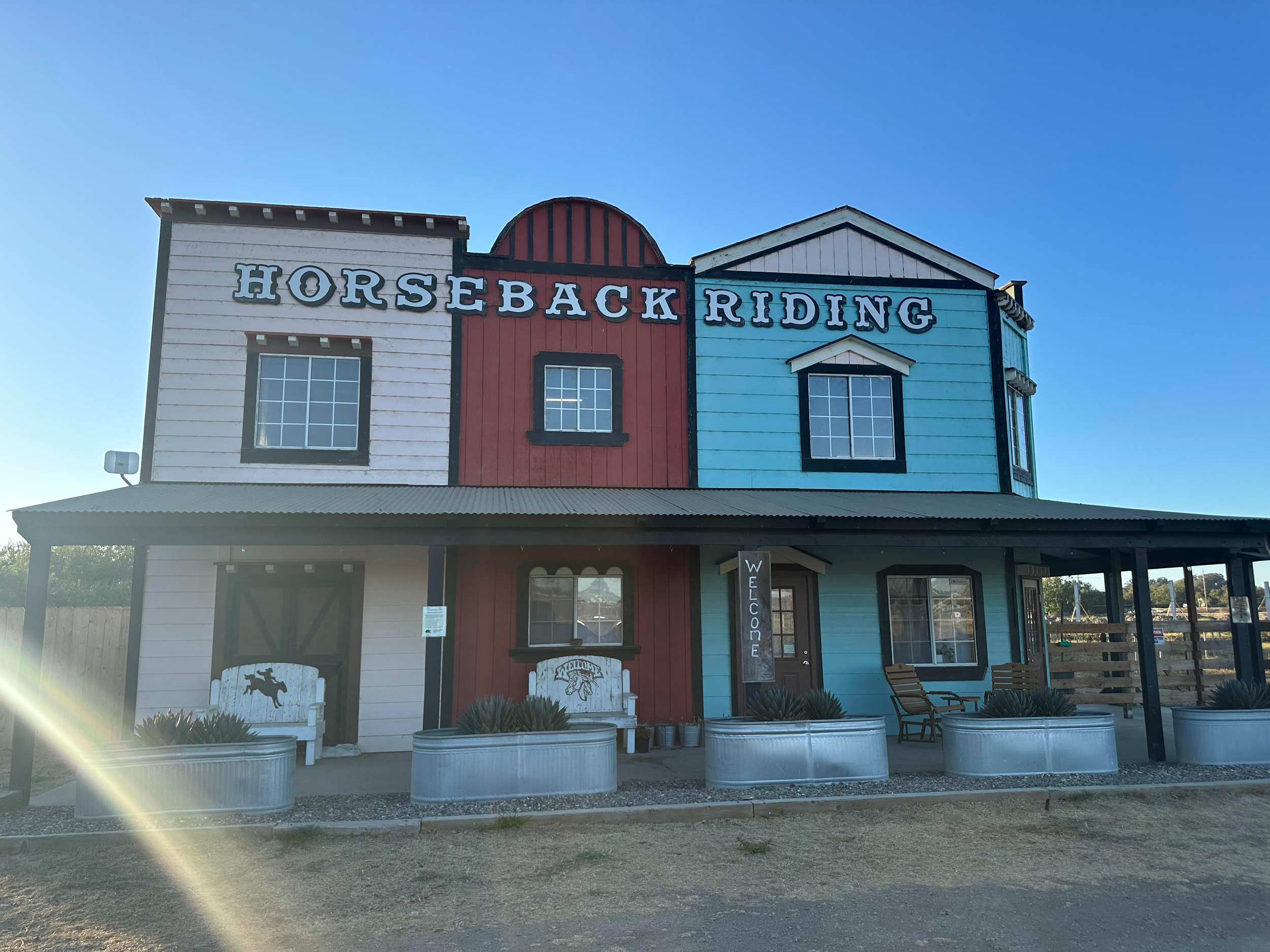 An old western-style building with 'Horseback Riding' signage and rustic architecture in warm sunlight.