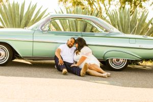 Couple sitting by mint green classic car surrounded by tropical plants.