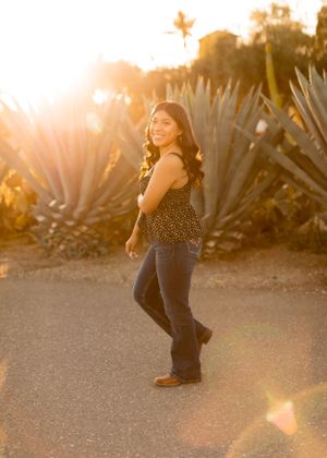 Someone wearing a polka dot top and jeans poses playfully near desert plants at sunset.