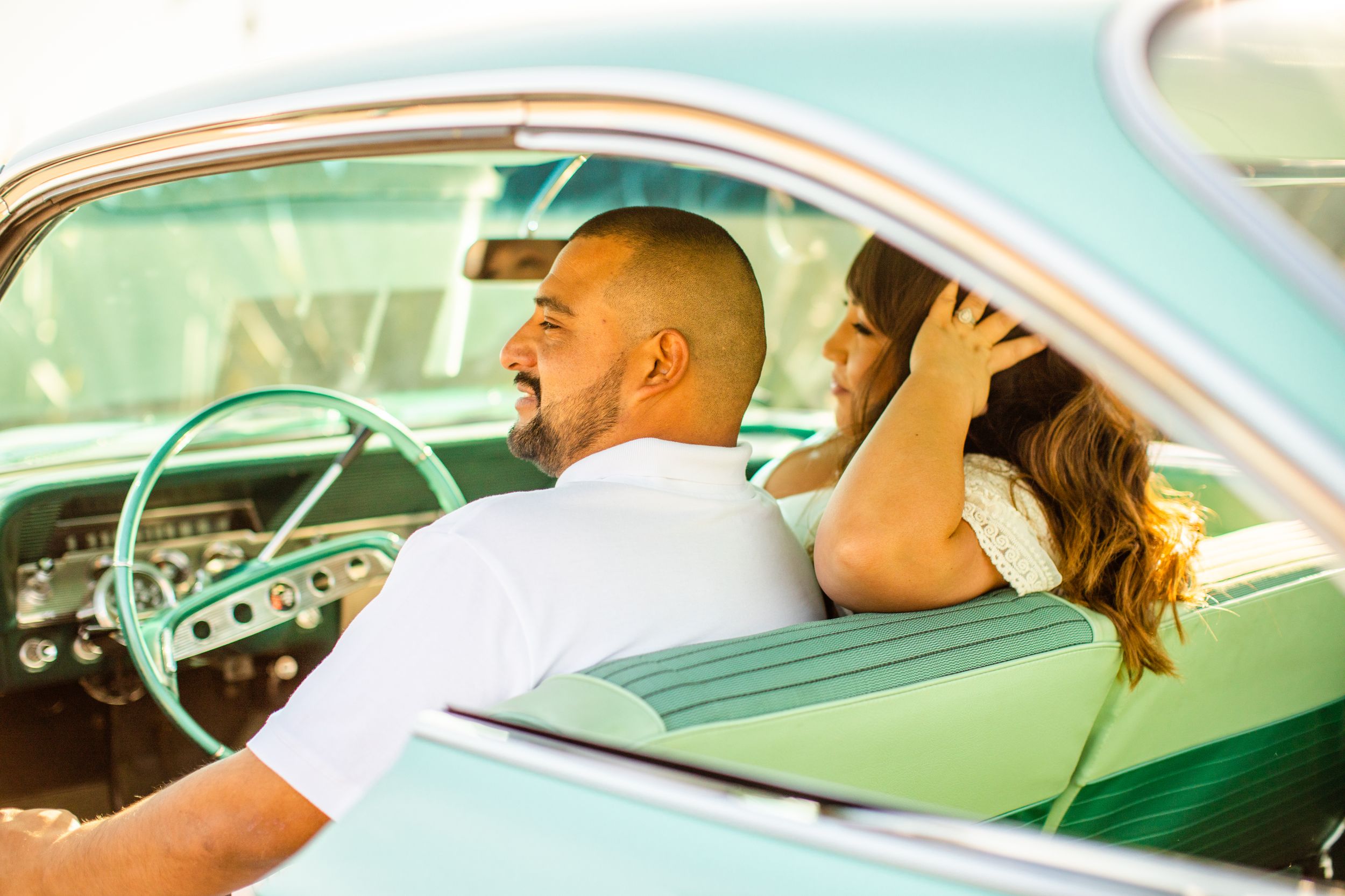 Couple enjoying ride in classic turquoise vintage car on sunny day.