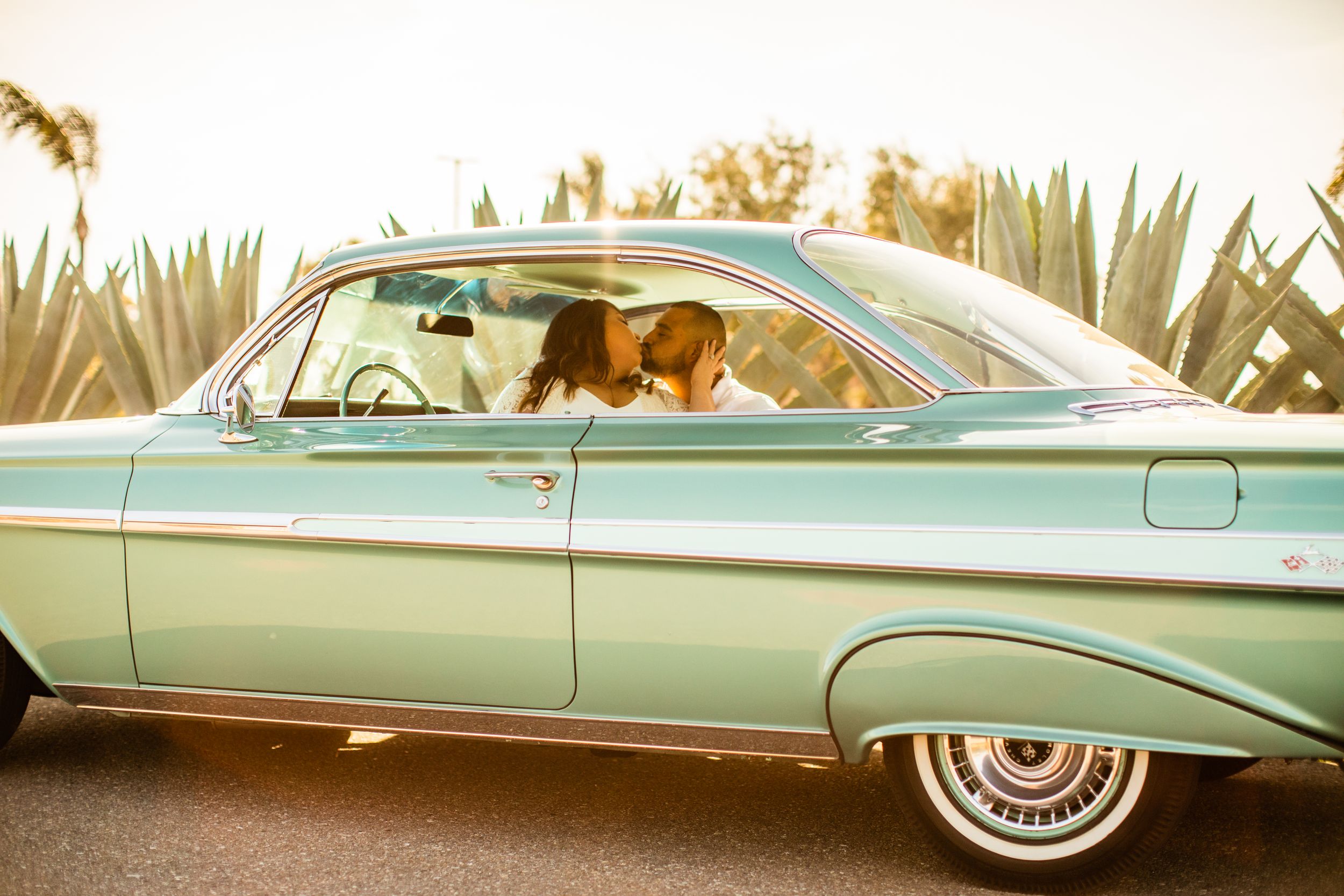 Vintage turquoise car parked with desert plants in background during golden hour.