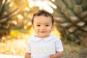 Joyful toddler wearing white shirt smiles brightly in outdoor setting with golden sunset bokeh.