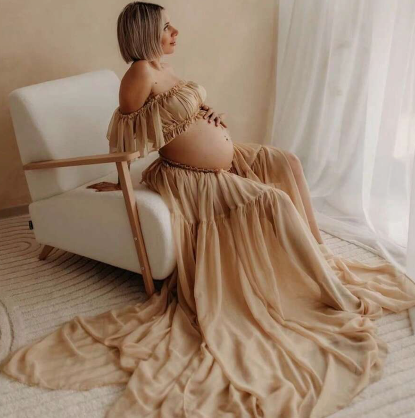 Artistic maternity photos with flowing beige dress on white bedding.