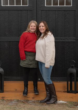 Two people in winter outfits pose against a black wall wearing cozy sweaters and boots.
